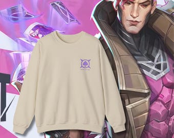 May include: A beige crewneck sweatshirt with a purple graphic on the chest. The graphic is a stylized spade within a circle, with text below. The background features a comic book illustration of a character with red hair and playing cards.