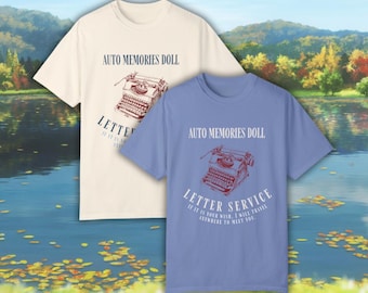 May include: Two t-shirts with a vintage typewriter graphic and the text "AUTO MEMORIES DOLL" and "LETTER SERVICE IF IT IS YOUR WISH, I WILL TRAVEL ANYWHERE TO MEET YOU." The t-shirt on the left is cream colored and the t-shirt on the right is light blue.