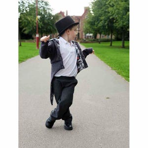 May include: A child in a black top hat, dark grey jacket with patterned lining, white collared shirt, and dark grey trousers. The child wears black shoes and walks on a paved path. The jacket has a long tail.