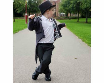 May include: A child in a black top hat, dark grey jacket with patterned lining, white collared shirt, and dark grey trousers. The child wears black shoes and walks on a paved path. The jacket has a long tail.