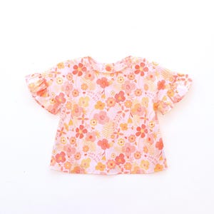 Könnte beinhalten: Ein kurzärmliges Oberteil mit einem Blumenmuster in Rosa, Orange und Gelb. Das Oberteil hat einen runden Ausschnitt und Rüschenärmel. Der Stoff ist leicht, möglicherweise Baumwolle oder ein ähnliches Material.