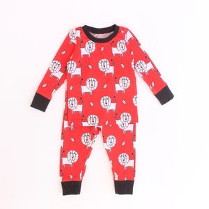 Pode incluir: Conjunto de pijama vermelho para crianças com estampa de leão branco. A parte superior de manga comprida e as calças têm punhos pretos e decote preto. O desenho do leão é repetido no tecido.