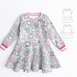 May include: A long-sleeved dress with a white background and a colorful heart and floral pattern. The dress has a pink trim around the neckline and cuffs. The cuffs also have stripes of pink, gray, and white. A diagram of the dress is in the upper right corner.