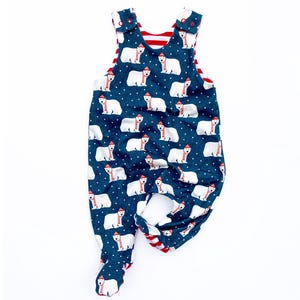 Può includere: Un pagliaccetto blu navy per bambini con un motivo ripetuto di orsi polari bianchi con cappelli e sciarpe rosse. Il pagliaccetto ha una fodera a righe rosse e bianche e chiusure con bottoni sulle spalle.