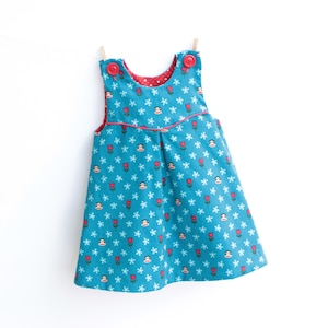 Könnte beinhalten: Türkisfarbenes Babykleid mit einem Blumenmuster aus roten Tulpen und weißen Sternen. Das Kleid hat ein rotes Futter mit weißen Punkten und roten Knöpfen. Das Kleid hängt an einer Wäscheleine vor weißem Hintergrund.