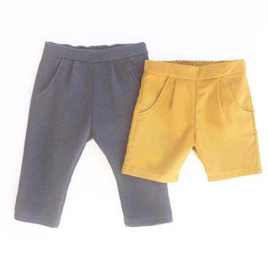 May include: Two pairs of children's bottoms. One pair is navy blue pants with pockets. The other is mustard yellow shorts with pockets. Both pairs have elastic waistbands and are made of a soft fabric.