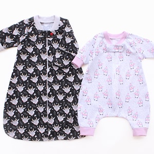 Puede incluir: Dos sacos de dormir para bebés. Uno es negro con un estampado de cabezas de ciervo y estrellas. El otro es gris claro con un estampado de figuras rosas. Ambos tienen mangas largas, cremalleras y están hechos de tela suave.