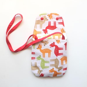 Puede incluir: Un bolso cruzado de tela blanca con una correa roja. El bolso tiene un estampado de ciervos coloridos en naranja, verde y rojo. El bolso tiene un cierre de solapa con un bot&oacute;n rojo.