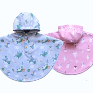 May include: Two hooded rain ponchos. One is light blue with a pattern of green dragons, clouds, and moons. The other is pink with a pattern of ballerinas. Both have button closures.