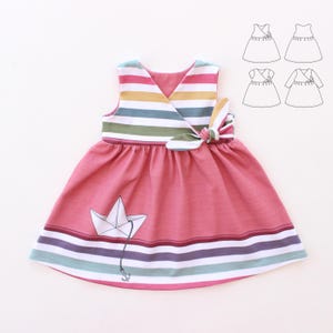 Peut inclure: Robe rose sans manches avec un corsage rayé et un motif de bateau en papier. Le corsage présente un col en V et un détail de nœud. La jupe a des rayures horizontales de différentes couleurs. Un motif de bateau en papier est sur la jupe.