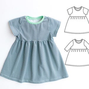 May include: A short-sleeved dress with a textured blue and white pattern, a green neckline, and a gathered waist. The image also includes two line drawings of the dress, showing short and long sleeve options. The dress is likely for children.