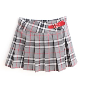 May include: A gray pleated skirt with a red and black plaid pattern. The skirt has a red belt with a silver buckle. The skirt is made of a soft material and is suitable for everyday wear.