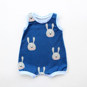 May include: A blue baby romper with white and light blue trim. The romper has a pattern of cartoon bunny faces with grey ears and pink noses. The sleeveless design and soft fabric suggest comfort for a baby or toddler.