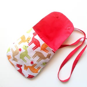 Puede incluir: Un bolso de hombro rojo y blanco con cierre de solapa. El bolso presenta un estampado de ciervos coloridos sobre un fondo blanco. El interior y la correa son rojos. El bolso tiene dos cierres a presi&oacute;n y una correa larga.