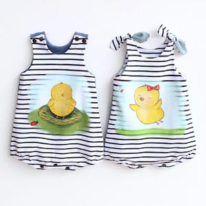 May include: Two baby rompers with a black and white striped pattern. One romper features a yellow chick in a nest, and the other has a chick with a red bow. Both have blue accents and are designed for infants.