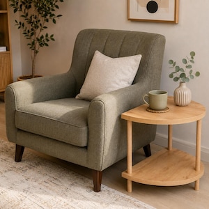 May include: An olive green upholstered armchair with vertical channel tufting on the backrest, featuring a light beige square throw pillow, positioned next to a semi-circular light wood side table with two tiers and four cylindrical legs.