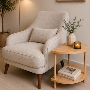 May include: An upholstered armchair in a light beige textured fabric with a matching rectangular lumbar pillow, supported by four dark brown tapered wooden legs, positioned next to a two-tiered semi-circular light wood side table.