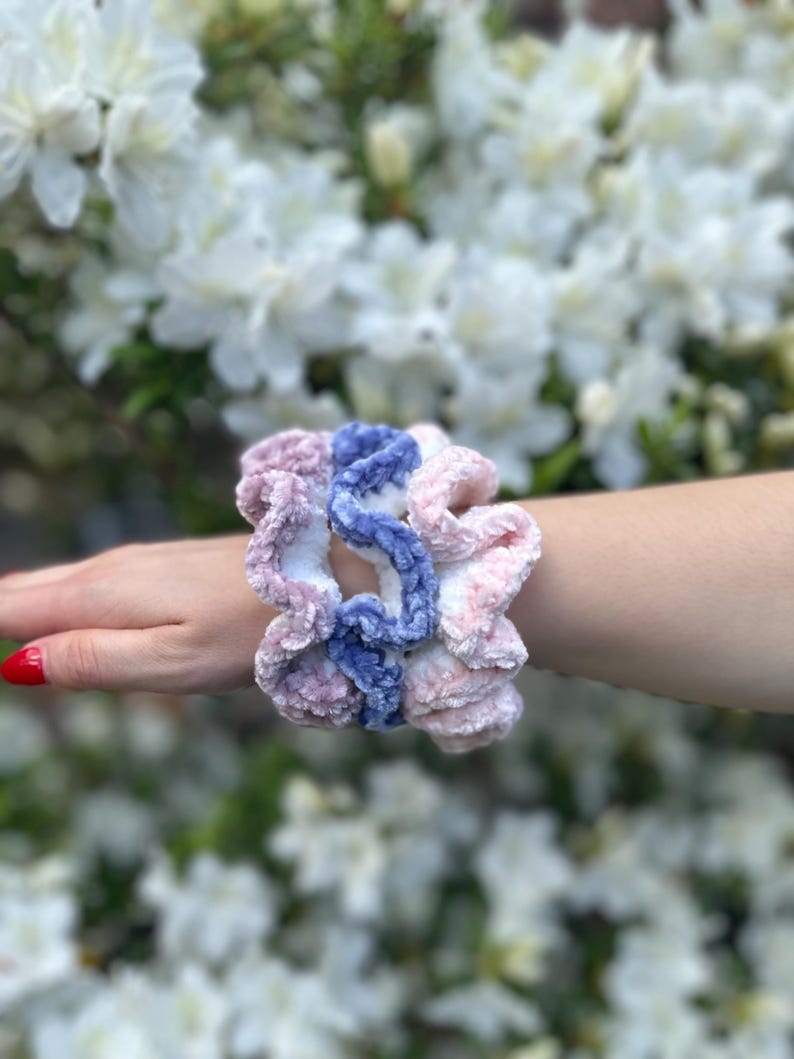 3 scrunchies made of soft, fuzzy yarn. One scrunchie is a dusty violet with white, one is light pink with white,  and the other is a light blue with white.