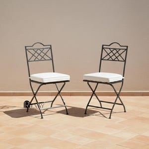 May include: Two black metal folding chairs with white cushions. The chairs have a diamond pattern on the backrests. The chairs are on a tiled surface.