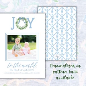 May include: A Christmas card design with the word "JOY" in light blue, a wreath, and a family photo. The card includes the text "to the world" and family details. The back features a blue and white pattern. Text: Personalized or pattern back available.