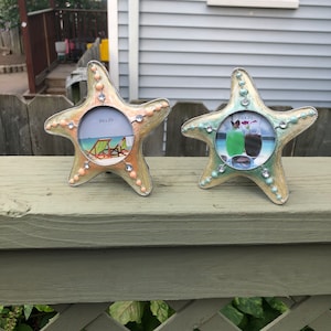 May include: Two starfish-shaped picture frames with a light blue and light pink finish. The frames are decorated with rhinestones and have a silver-colored metal frame. The frames are 2 1/2 x 2 1/2 inches.