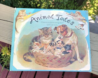 May include: A vintage children's book titled "Animal Tales" by Ernest Nister. The cover features a colorful illustration of a cat, a dog, and a basket of kittens and puppies.
