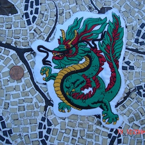 May include: Green and red embroidered iron-on patch of a dragon with a yellow and gold outline. The dragon is curled up with its tail in its mouth.