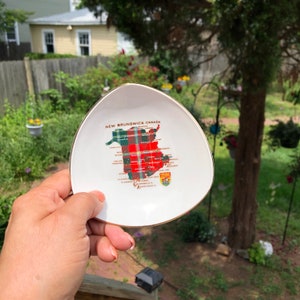 May include: A white ceramic dish shaped like the province of New Brunswick, Canada. The dish is decorated with a red and green tartan pattern and the words "New Brunswick Canada".