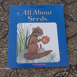 May include: A blue book titled "Now I Know All About Seeds" with an illustration of a chipmunk holding an acorn. The book is published by Troll Associates.