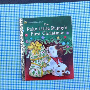May include: A Little Golden Book titled "The Poky Little Puppy's First Christmas". The cover features a brown and white puppy with black spots, wearing a red bow, looking at a Christmas stocking filled with presents.