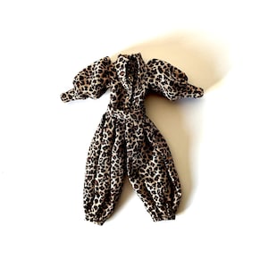 May include: A leopard print jumpsuit with a belted waist and puffed sleeves. The one-piece garment features a brown and black spotted pattern. The jumpsuit is laid flat on a white surface.