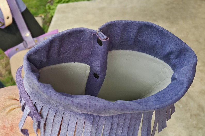 K&ouml;nnte beinhalten: Lilafarbene Wildledertasche mit Fransenbesatz und Druckknopfverschluss. Die Tasche ist mit hellem grauen Stoff gef&uuml;ttert.