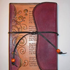 Op de afbeelding: Een bordeauxrood lederen dagboek met een tan lederen omslag met een decoratief bloemmotief en een gedicht met de titel "BLIND". Het dagboek is gesloten en vastgebonden met een zwart lint.