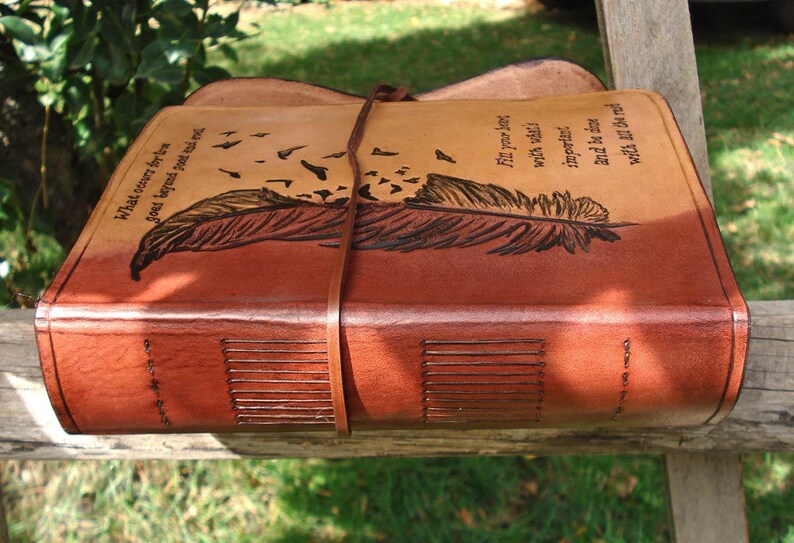 Op de afbeelding: Een bruin lederen dagboek met een verenontwerp en de quote "What is cover for love goes beyond good and evil."  Fit your journey with what's important. And be the wind while all the rest...
