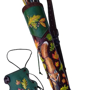 May include: A leather archery set, comprising a quiver and armguard. The quiver showcases a fox and autumn leaf design in brown, green, and orange. The set includes a brown leather strap and a matching armguard, perfect for archers.