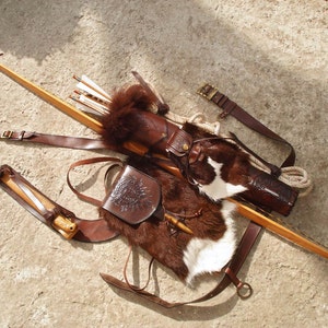 May include: A brown leather quiver with a fur-lined flap, a wooden bow, and a brown leather belt with a pouch. The quiver is decorated with a metal buckle and a leather strap.