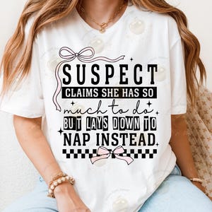 May include: White t-shirt with a black and white graphic that says "SUSPECT CLAIMS SHE HAS SO much to do. BUT LAYS DOWN TO NAP INSTEAD."