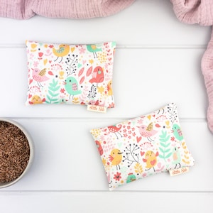 May include: Two white fabric heat packs with a colourful bird and floral pattern. The packs are labelled "Little Seb".