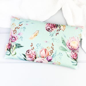 May include: A light green pillow with a floral pattern featuring pink, red, and yellow proteas. The pillow is on a white surface.
