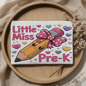 May include: A white rectangular zippered pouch featuring a cartoon pencil with a pink polka-dot bow, a smiling face, and the text Little Miss Pre-K in pink lettering. The design is surrounded by small colorful hearts and star-shaped accents.