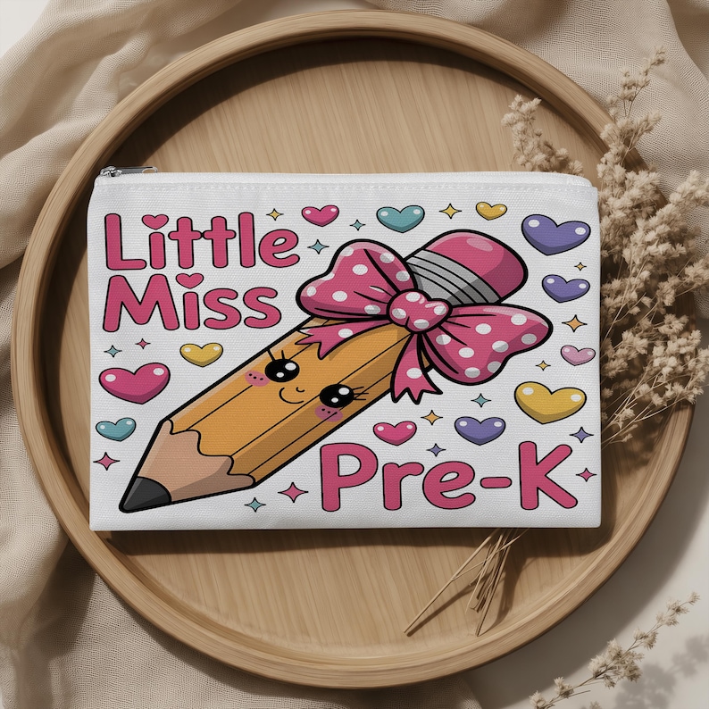 May include: A white rectangular zippered pouch featuring a cartoon pencil with a pink polka-dot bow, a smiling face, and the text Little Miss Pre-K in pink lettering. The design is surrounded by small colorful hearts and star-shaped accents.