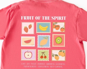 Może przedstawiać: Koralowa koszulka z nadrukiem ilustracji owoców na kwadratach przypominających znaczki pocztowe. Nad kwadratami znajduje się napis "FRUIT OF THE SPIRIT", a pod nimi słowa takie jak "MIŁOŚĆ" i "ŻYCZLIWOŚĆ". Koszulka jest wykonana z miękkiego materiału.