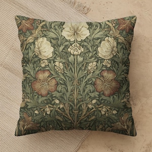 May include: A square throw pillow featuring a dense botanical pattern of cream, rust-red, and sage-green flowers and foliage. The symmetrical design displays large central blossoms surrounded by intricate leaves and smaller buds on a dark green background.