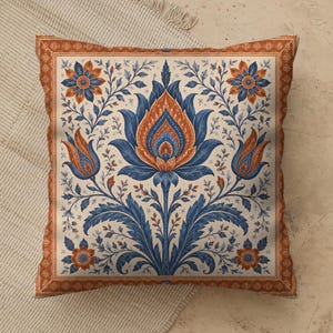 May include: A square throw pillow featuring a symmetrical floral pattern in shades of deep blue and burnt orange on a cream background. The design includes a large central lotus-like flower, smaller side buds, and a decorative border frame.