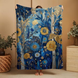 Puede incluir: Una manta floral azul y dorada. La manta presenta un diseño detallado de árboles y flores estilizados en tonos de azul, dorado y blanco. El diseño tiene una apariencia texturizada y artística, adecuada para la decoración del hogar.