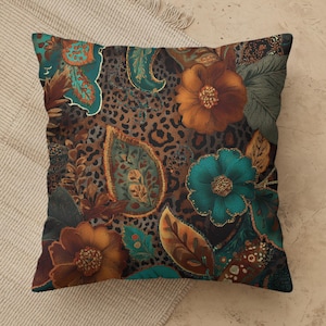 May include: A square throw pillow featuring a complex pattern of large orange and teal flowers, green leaves, and paisley shapes layered over a brown and black leopard print background. The design incorporates intricate textures and bold colors.