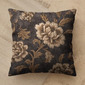 May include: A square throw pillow featuring a dark charcoal gray background with a woven floral pattern in shades of metallic gold and beige. The design displays large, detailed peony-like blossoms and leafy stems across the entire surface.