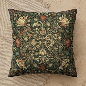May include: A square throw pillow featuring a symmetrical botanical pattern with cream, orange, and deep green foliage on a dark background. The design includes intricate floral motifs and swirling leaves arranged in a repeating, mirrored layout.
