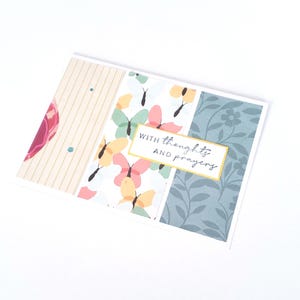 May include: A rectangular greeting card featuring three vertical panels. The left panel has beige stripes, the center panel displays colorful butterflies, and the right panel shows a blue floral pattern. A gold-bordered label reads WITH THOUGHTS AND PRAYERS.