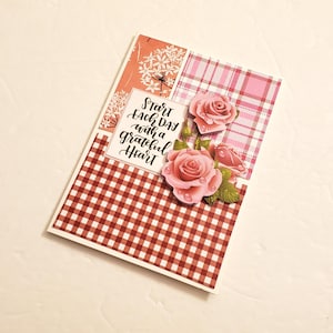 May include: A greeting card with a red and white gingham pattern and a pink floral design. The card has the text "Start Each Day with a Grateful Heart" written on it.